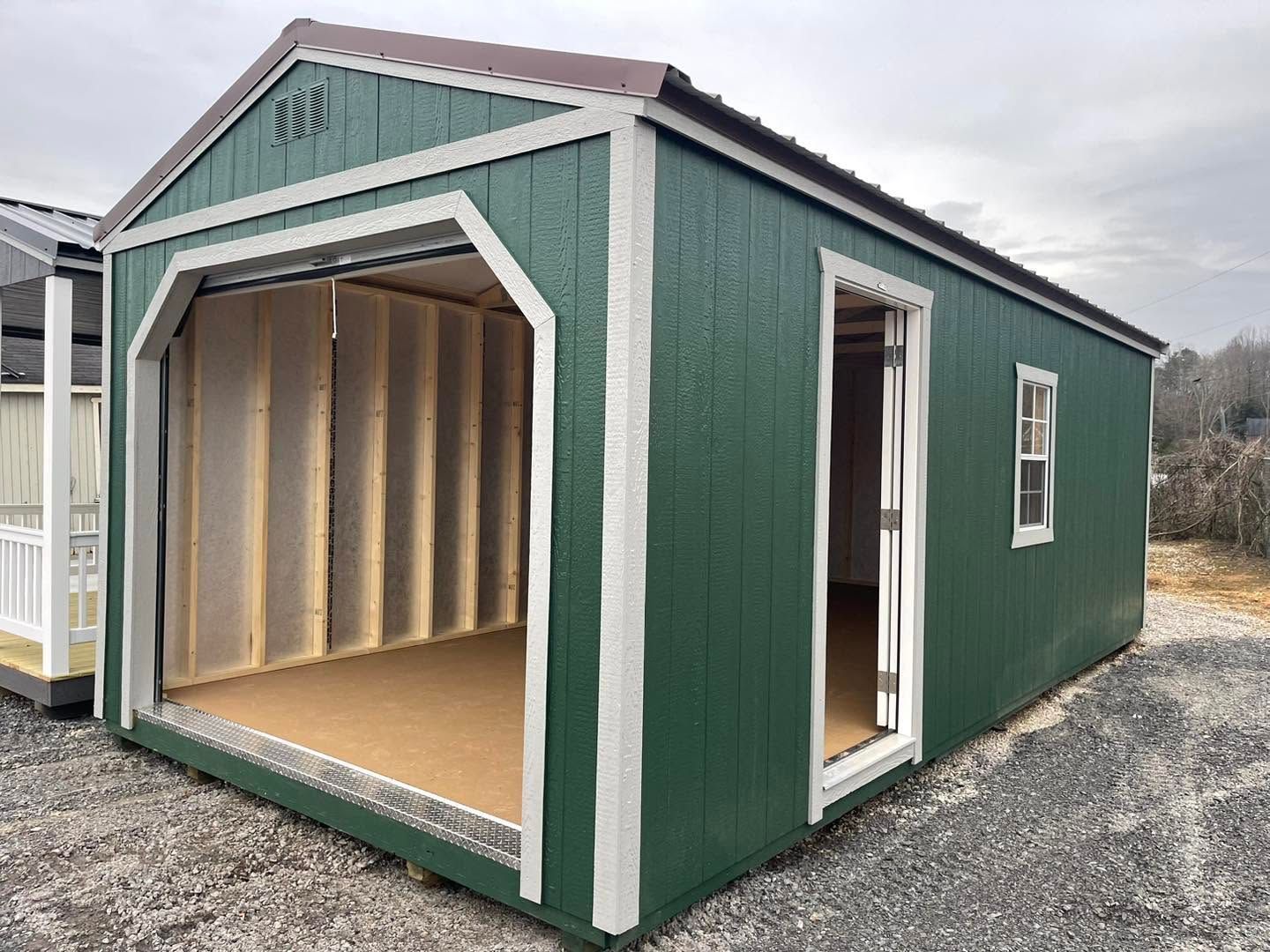 Green and white shed-style storage building with an open front and side door on gravel.