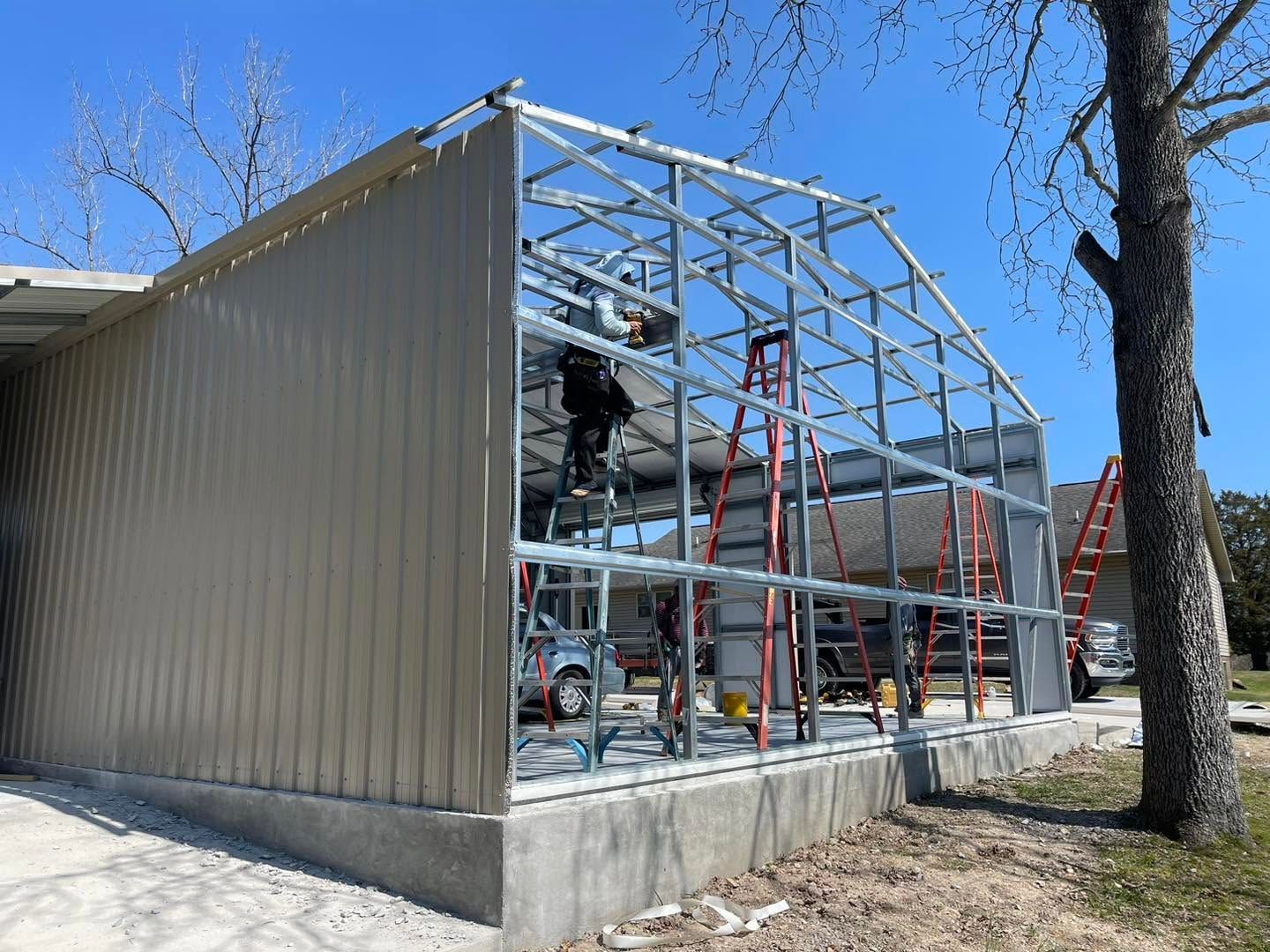Partially built metal-framed building beside a gray corrugated wall under a blue sky