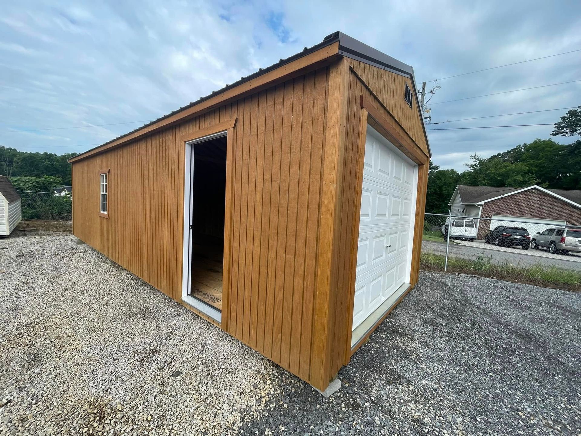 Wood-sided garage with an open side door and white roll-up door on a gravel lot
