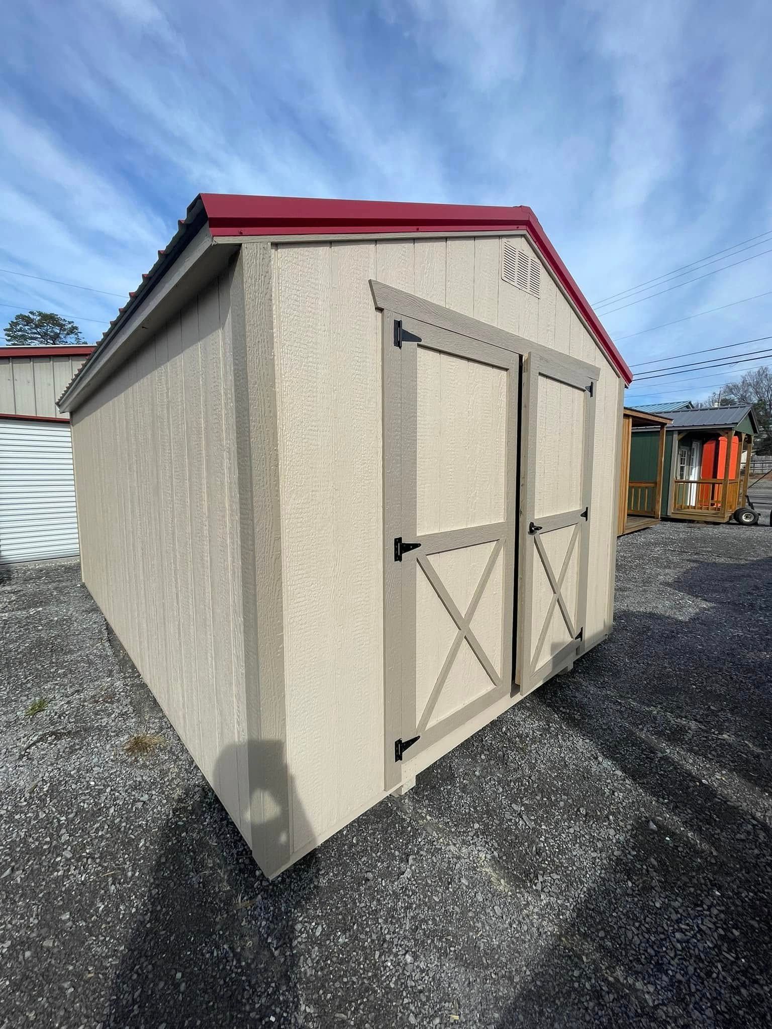 Beige garden shed with red roof and double doors on gravel under a blue sky