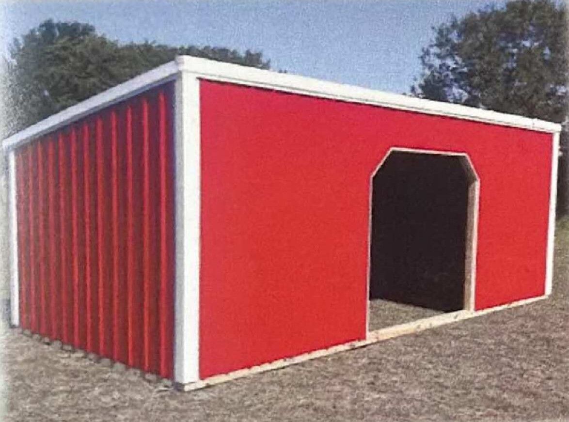 Red metal shed with white trim and an open doorway on a gravel lot