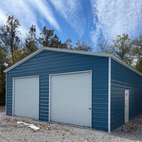 Blue metal storage building with two white roll-up garage doors and a side entry door