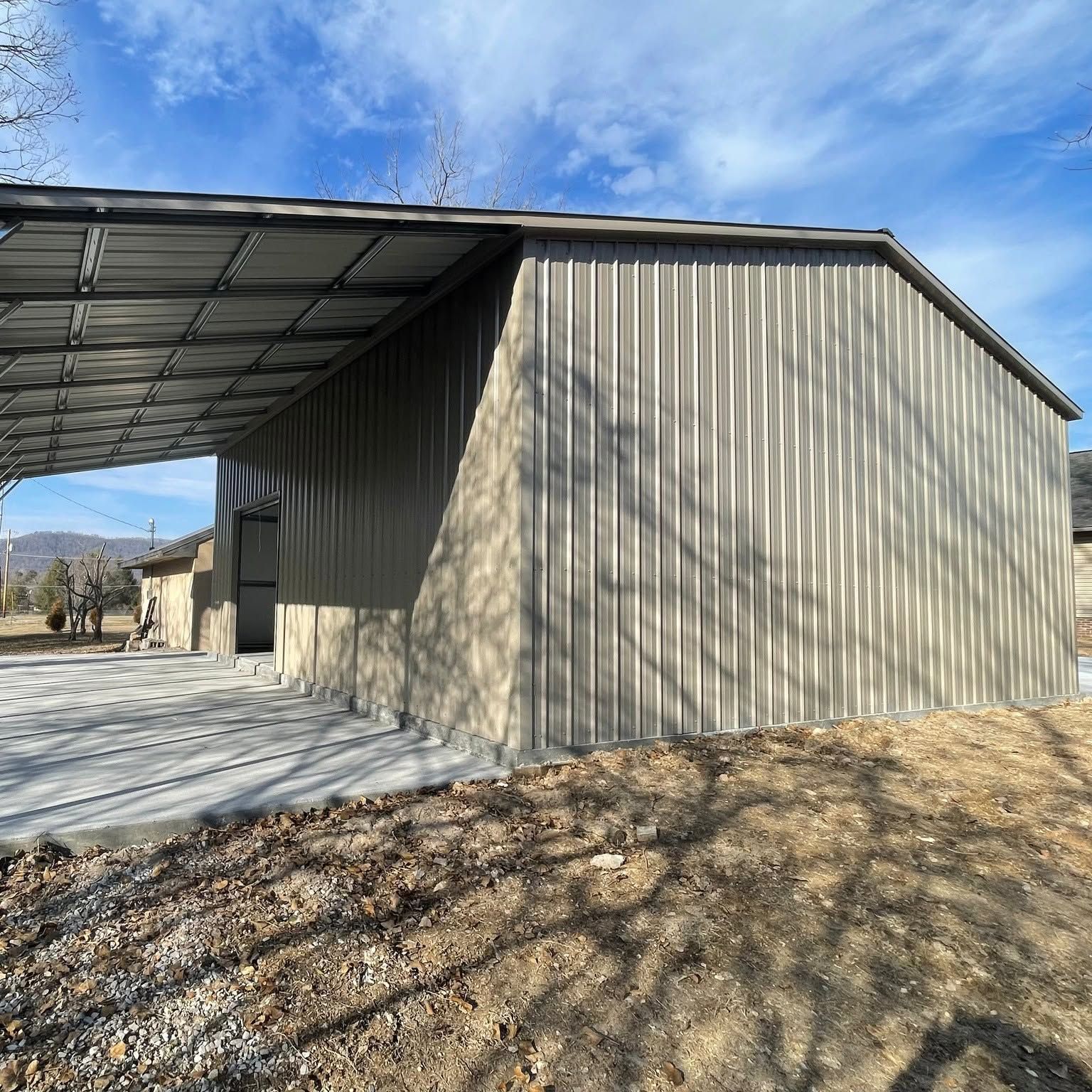 Metal building with a covered concrete entrance and shadowed siding under a blue sky