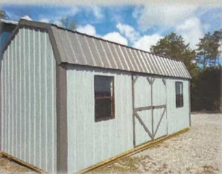 Small gray metal shed with a gabled roof, windows, and barn-style doors on a gravel lot