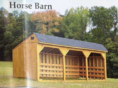 Wooden horse barn with gray roof and open front, set in a grassy field with trees behind.
