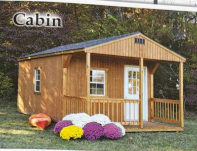 Small wooden cabin with porch, white trim, and colorful flowers on the lawn