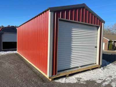 Red metal storage building with a closed white roll-up door on gravel