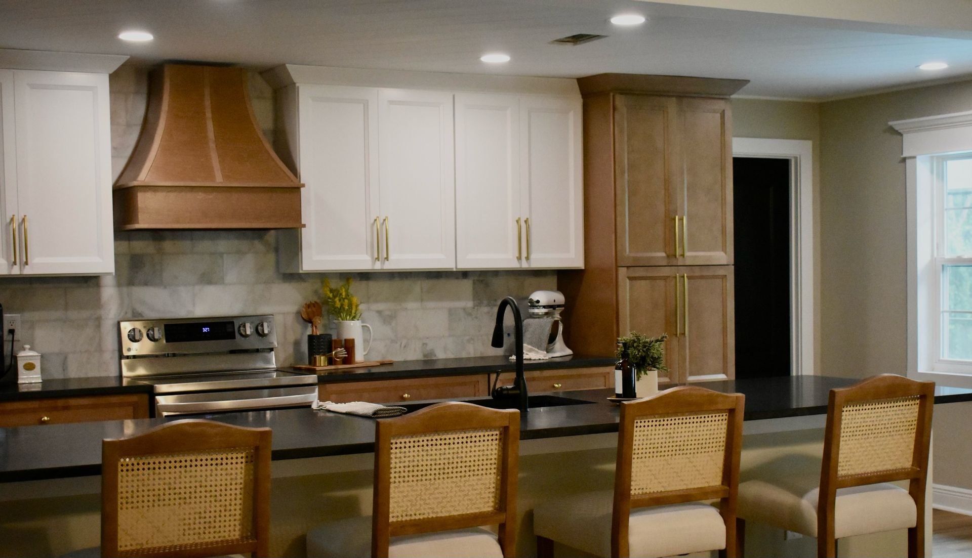A kitchen with white cabinets , black counter tops , a stove and a hood.