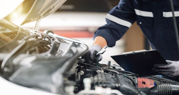 Mechanic working under an open car hood in a garage, with tools and engine parts visible
