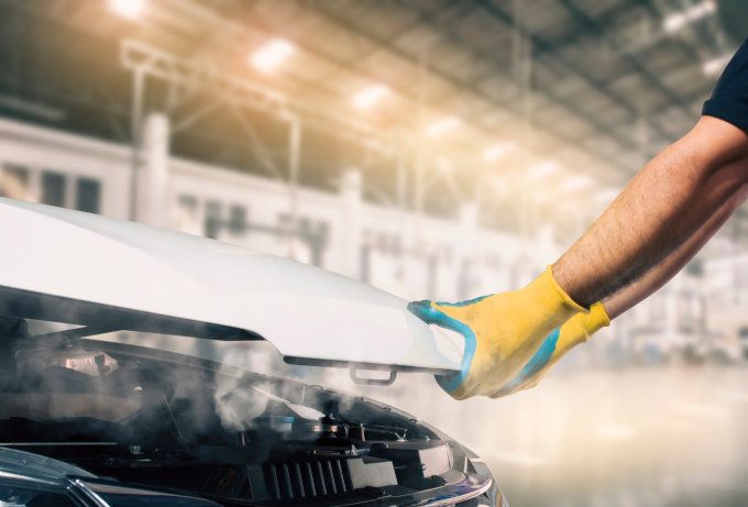 Gloved hand polishing a white car hood in an auto workshop