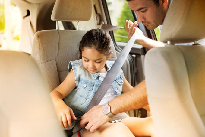 Adult buckling a child into a car seat in a beige car interior
