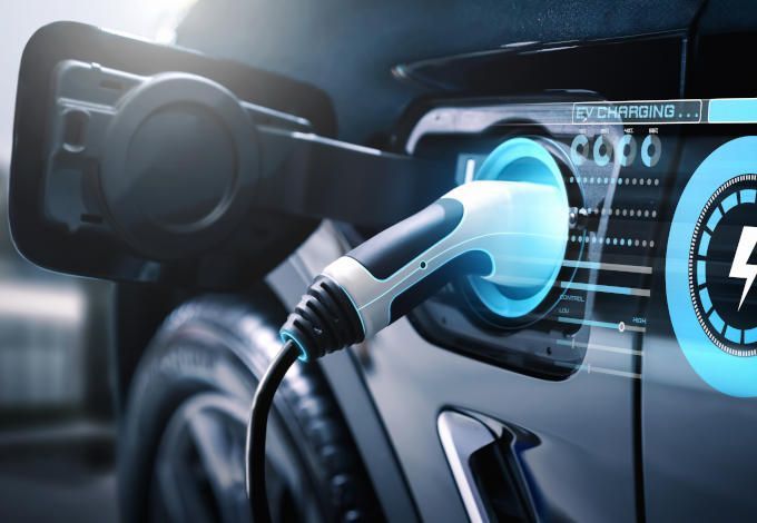 Electric car charging plug connected to a blue-lit vehicle charging port on a dark background