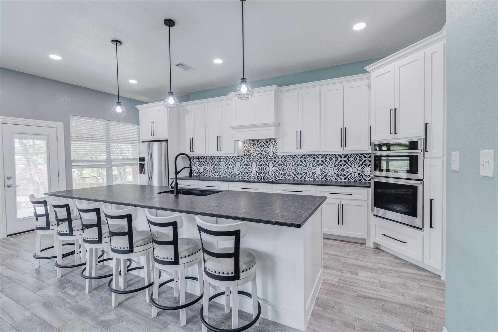 A kitchen with white cabinets , black counter tops , and a large island.