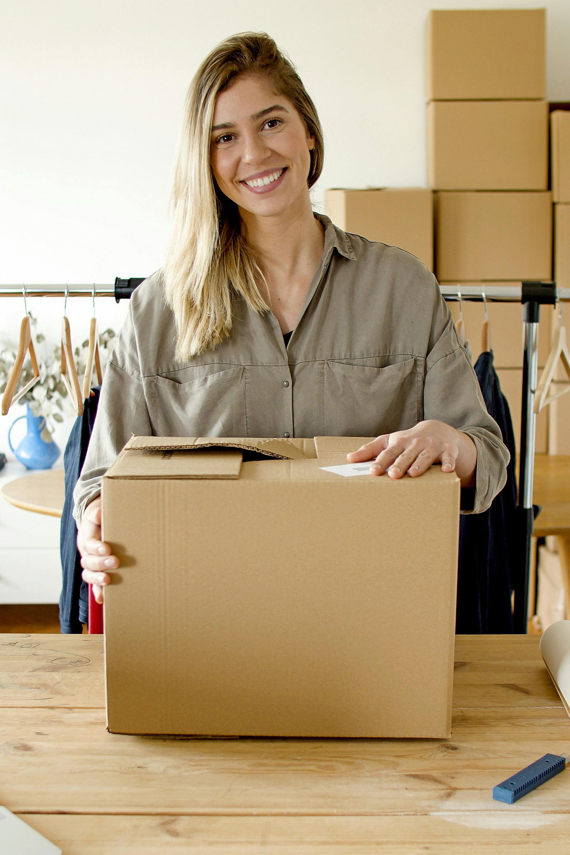 A woman is standing at a table holding a cardboard box she's packing for a move.