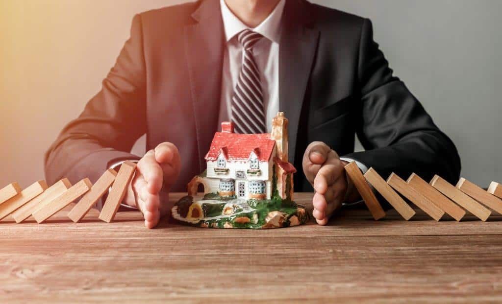 A man in a suit and tie is sitting at a table holding a model house and a car.