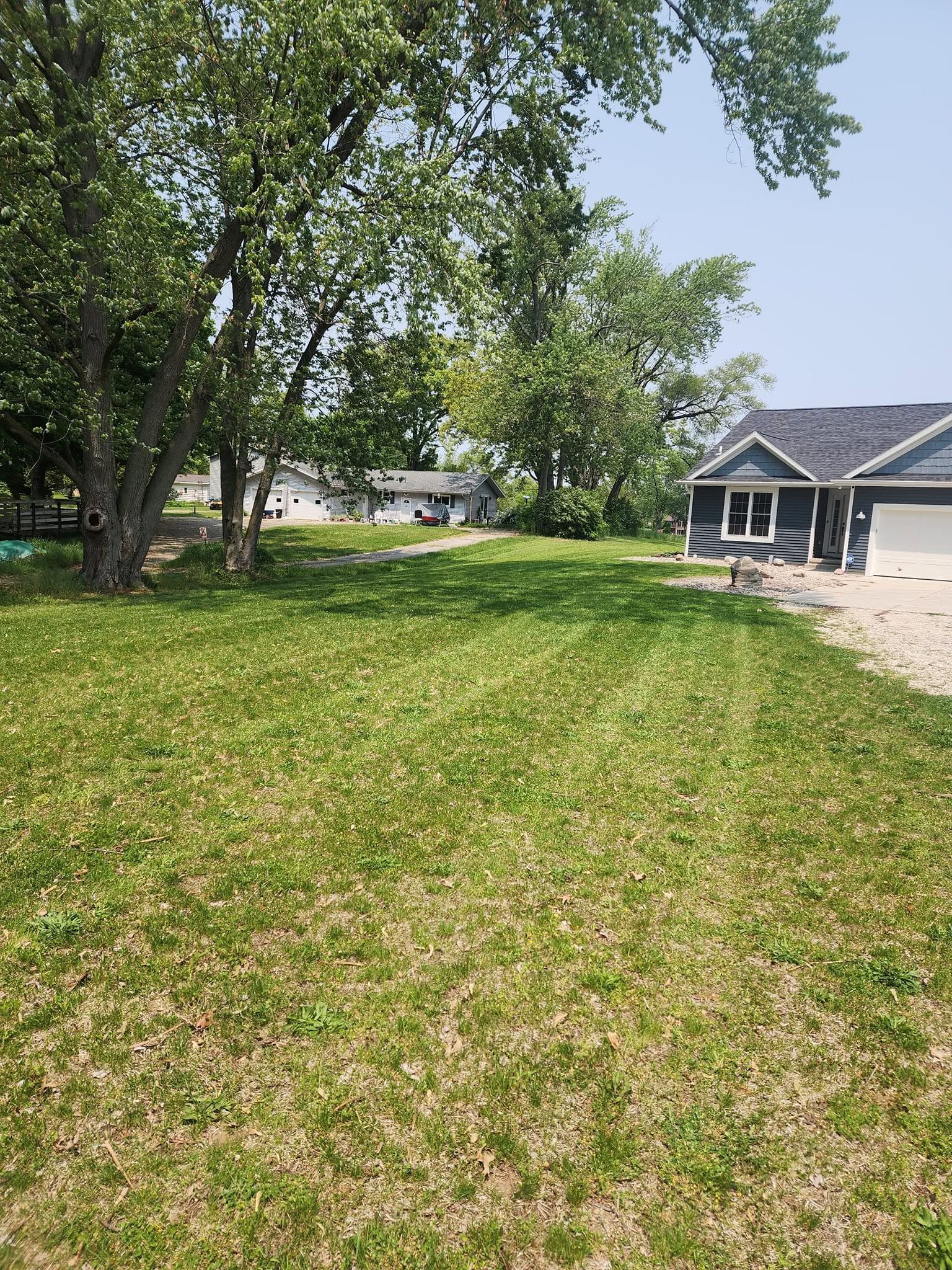 Grassy yard with trees and a gray house under a sunny sky