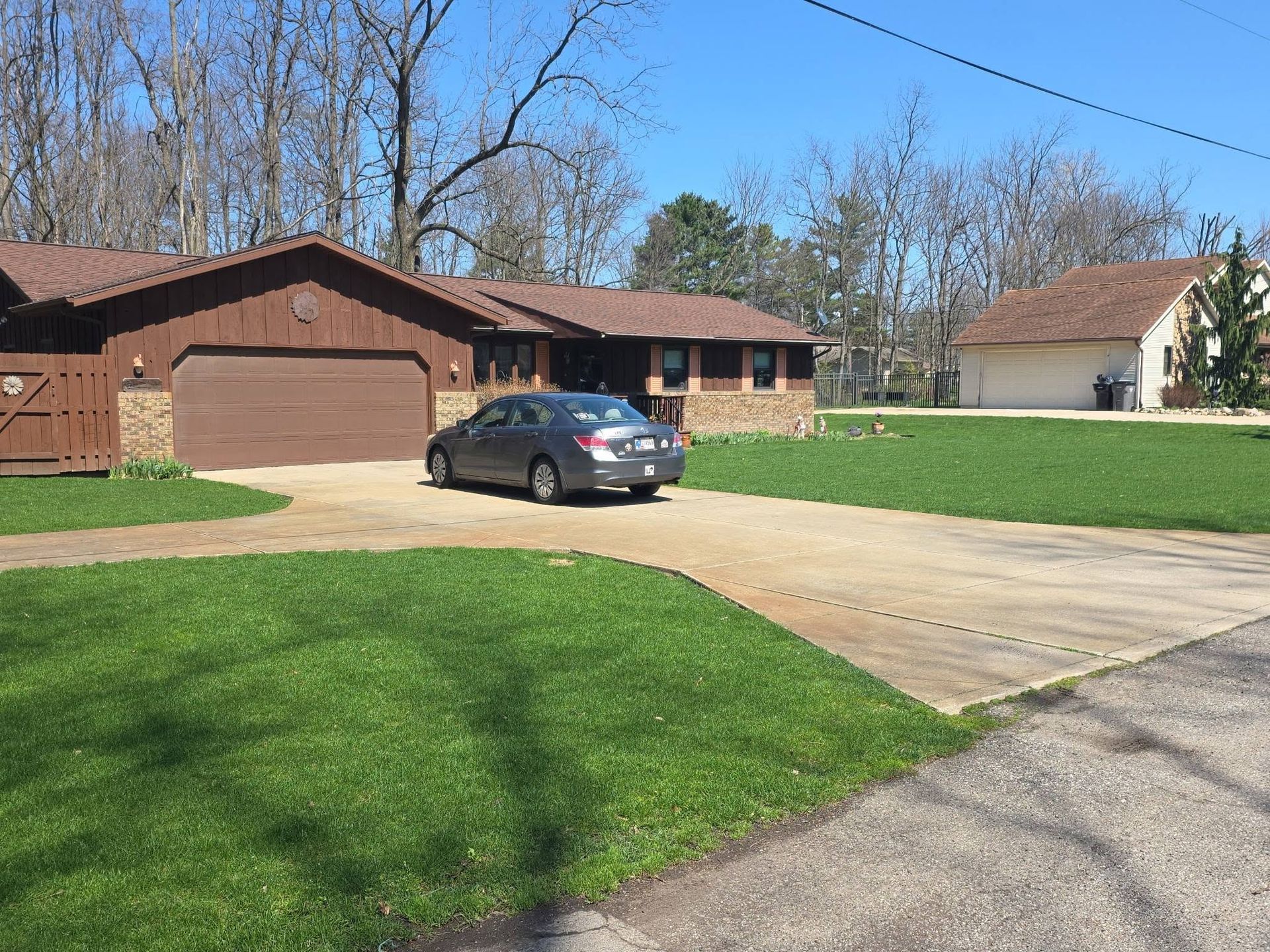 Suburban house with a two-car garage, a parked gray sedan, and a wide driveway under a clear sky
