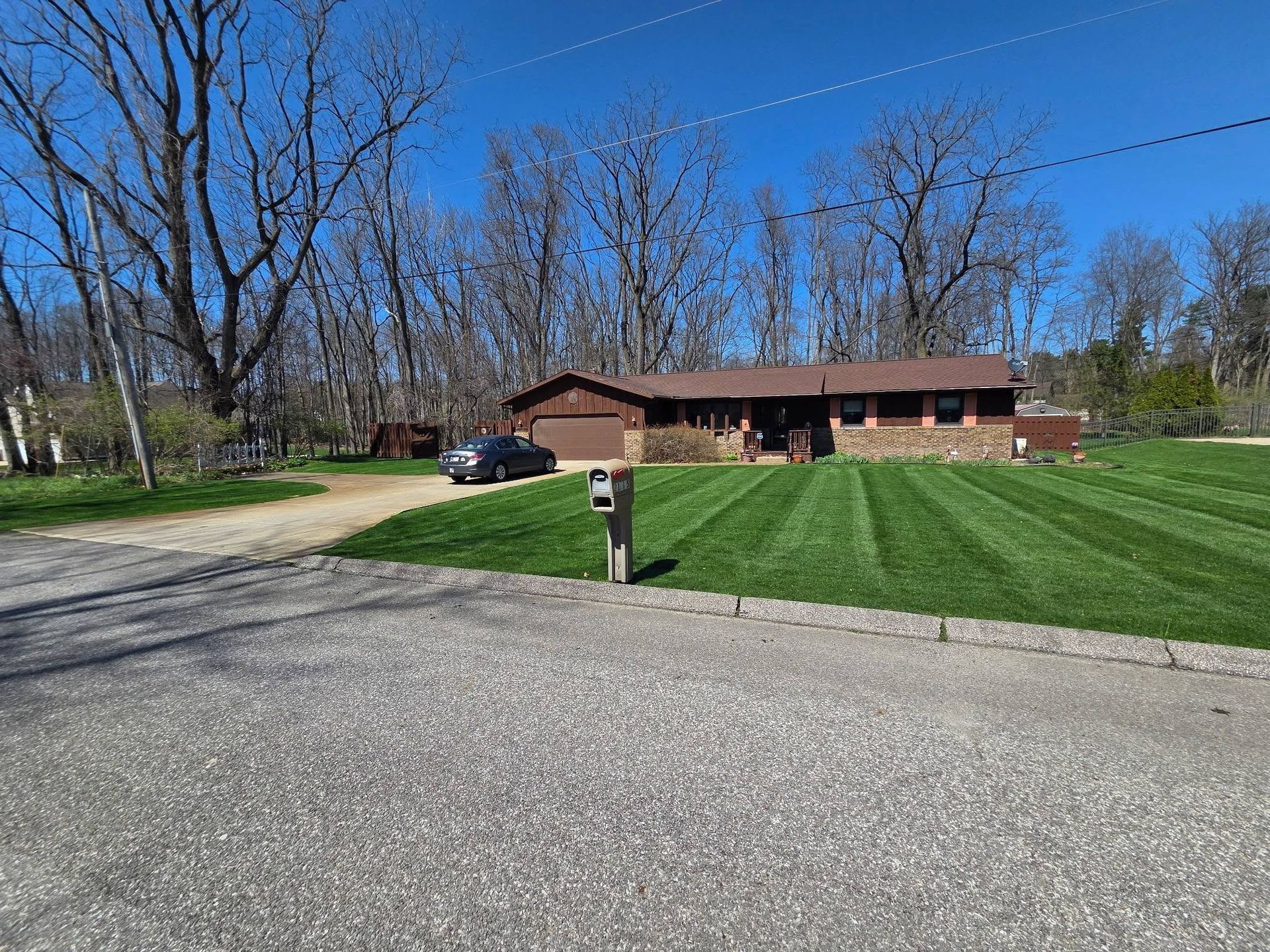 Suburban brick house with a manicured lawn, driveway, parked car, and mailbox under a clear blue sky