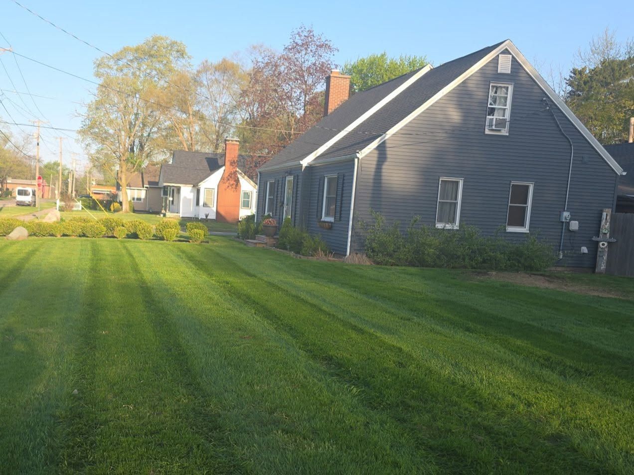 Suburban houses beside a wide green lawn under a clear sky, with autumn trees in the background