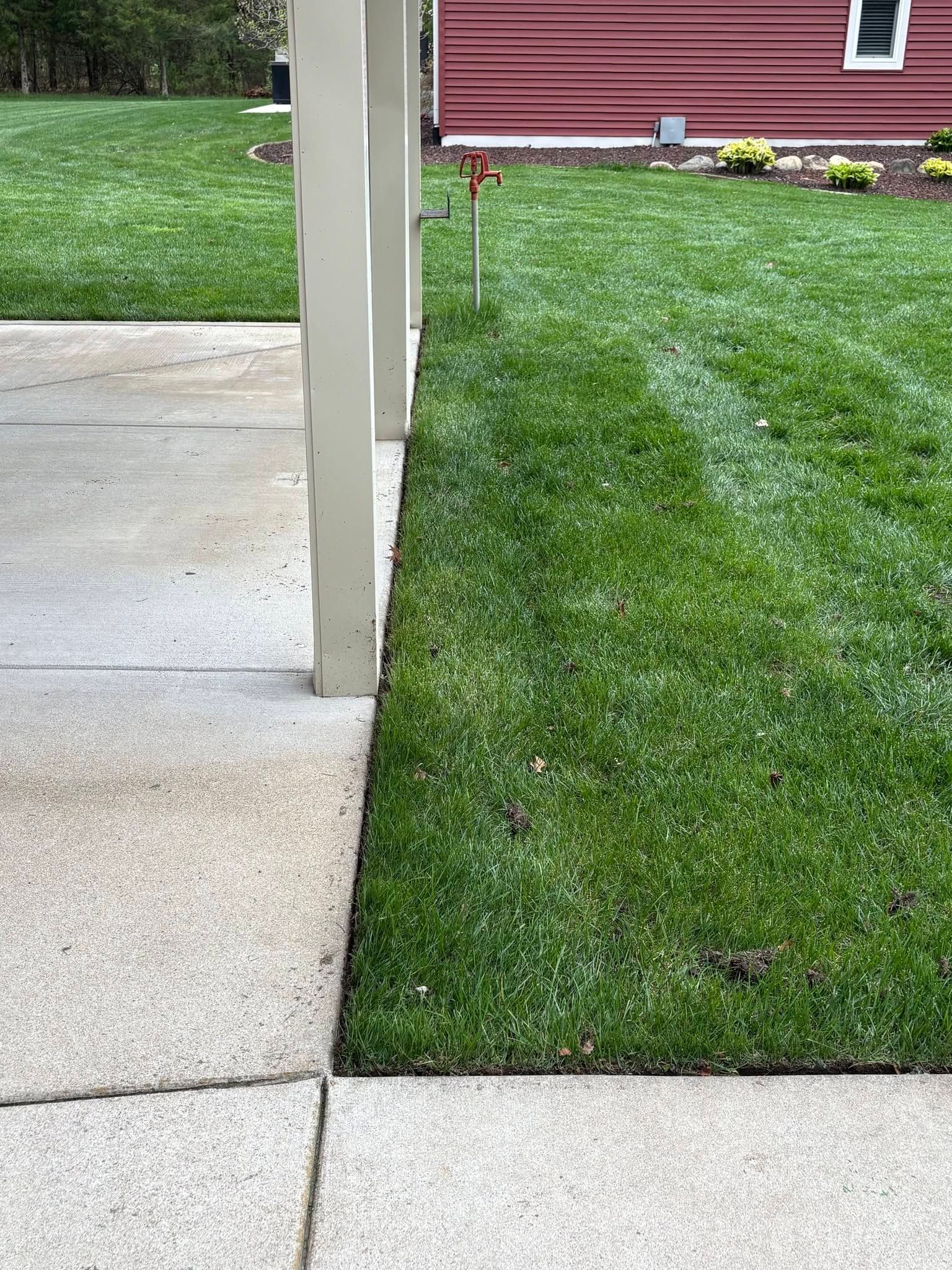 Concrete patio beside a green lawn and white post, with a red building in the background.