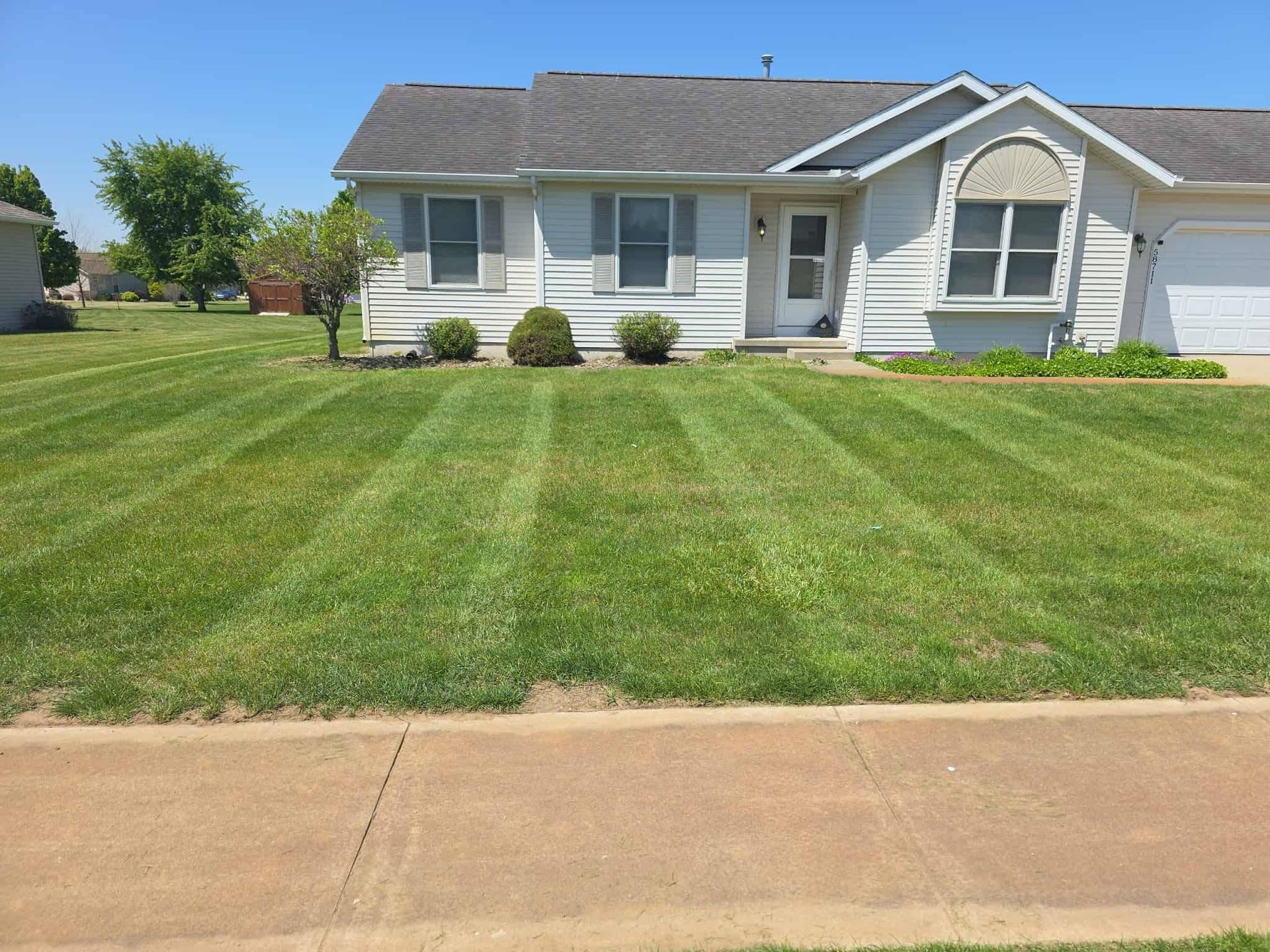 Single-story suburban house with a large green lawn and concrete sidewalk in front