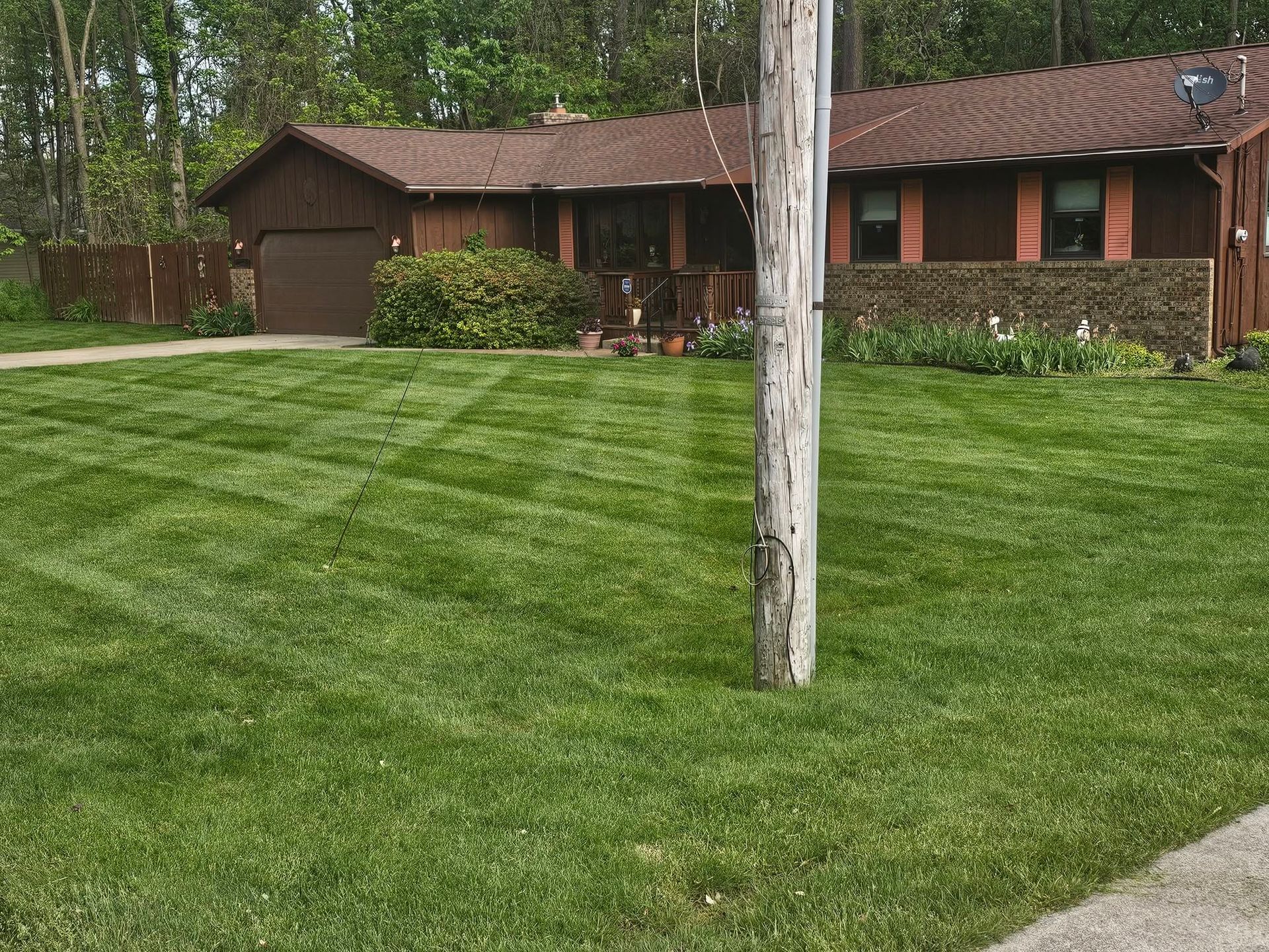 Single-story brick house with a neatly mowed lawn and a tree trunk in the foreground.