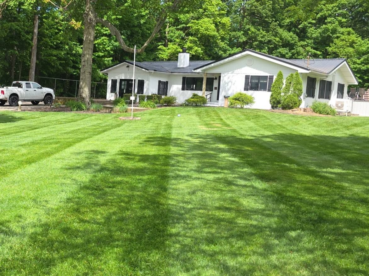 White ranch house with a striped green lawn, trees, and a parked pickup truck nearby.