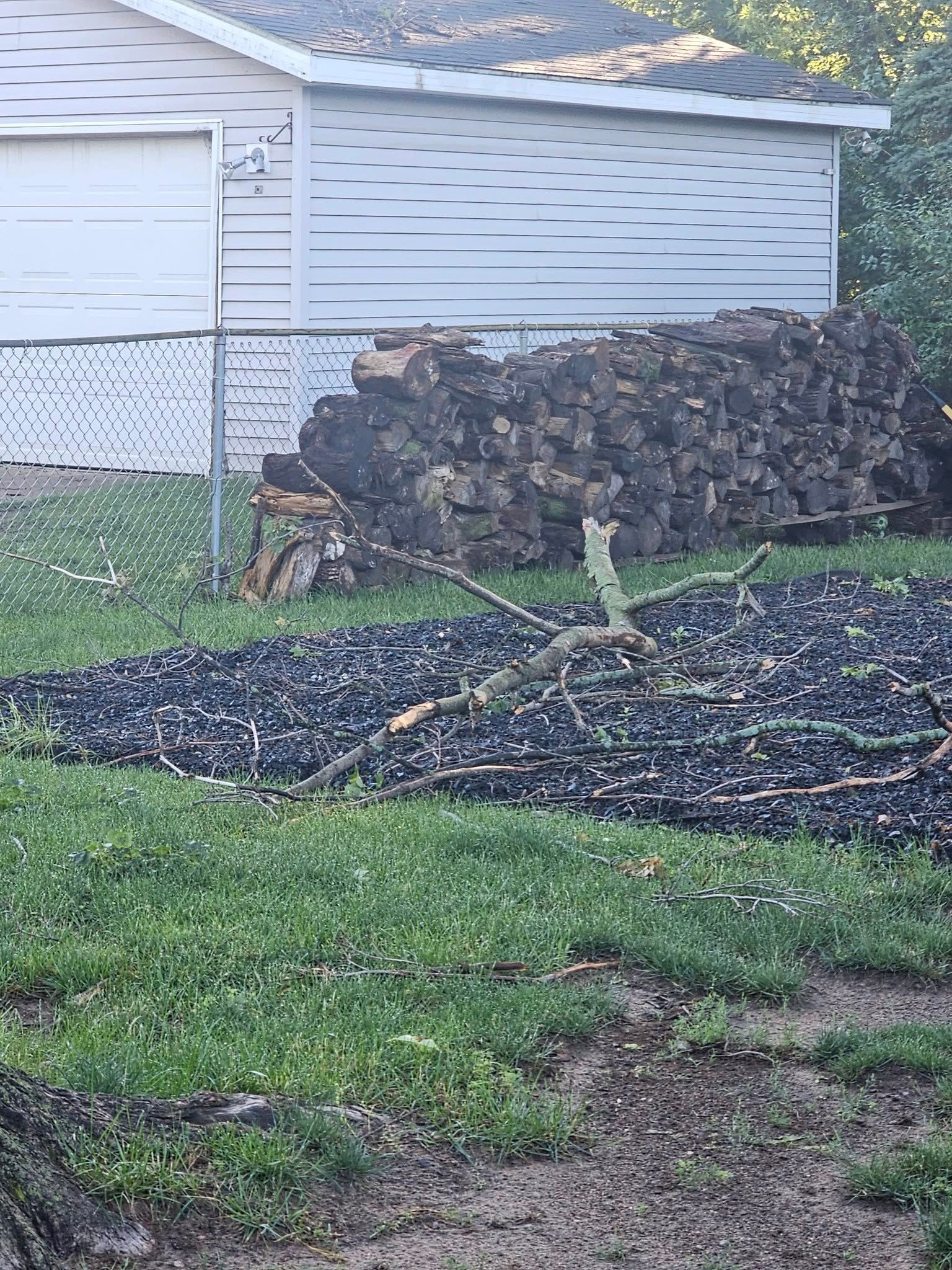 Storm-damaged yard with fallen black debris piled beside a house and fence