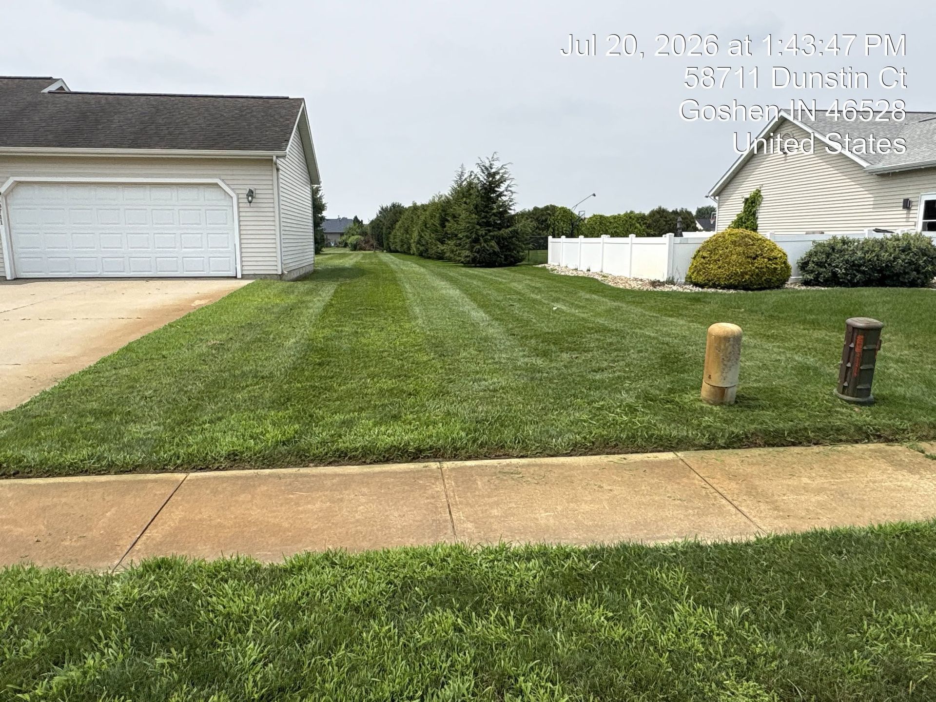 Suburban front yard with a green lawn beside a white garage and sidewalk, under a cloudy sky