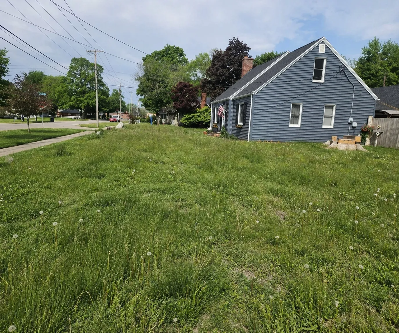Blue house with a grassy yard beside a street and sidewalk under a sunny sky