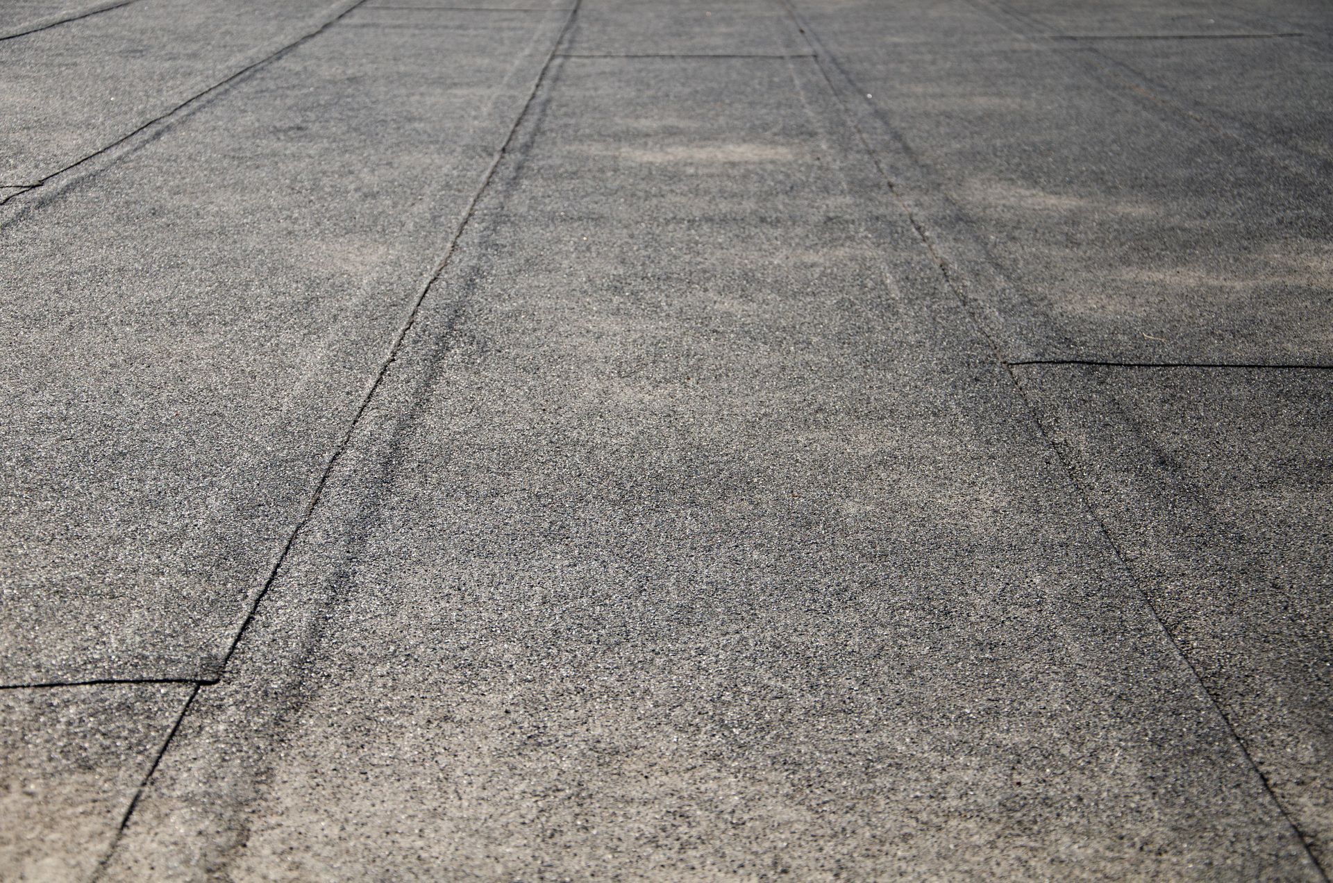Close-up of weathered gray pavement with cracks and texture in sunlight