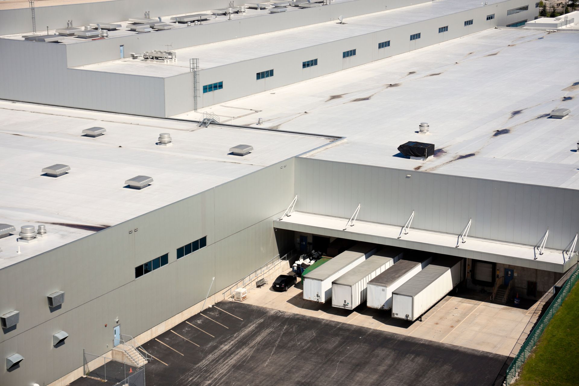 Aerial view of a large white warehouse with a loading dock and several white trucks parked outside.