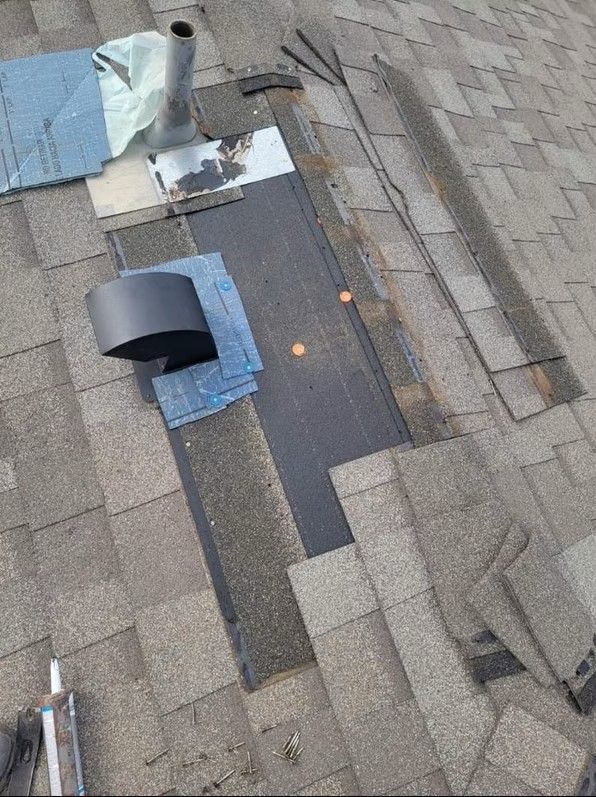 Roof shingles with a damaged area patched by blue tape and black roofing material