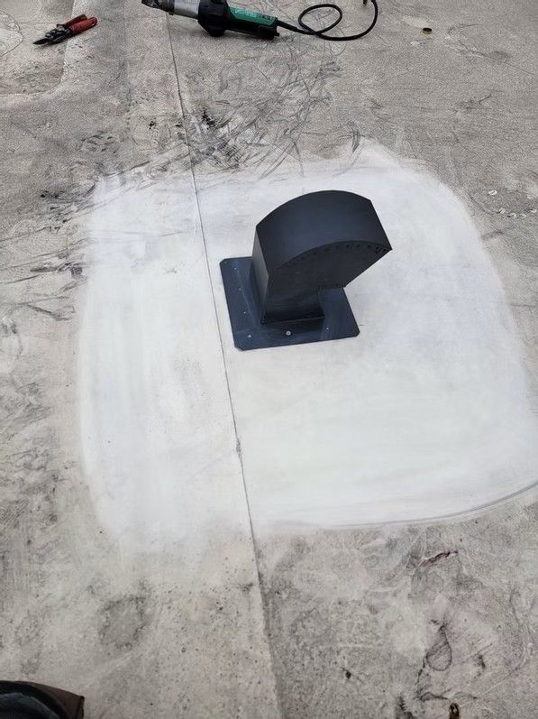 Small black rooftop vent on a white patched surface with tools nearby