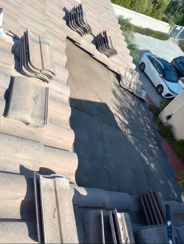 Roof with damaged shingles and debris near a driveway with two parked cars.