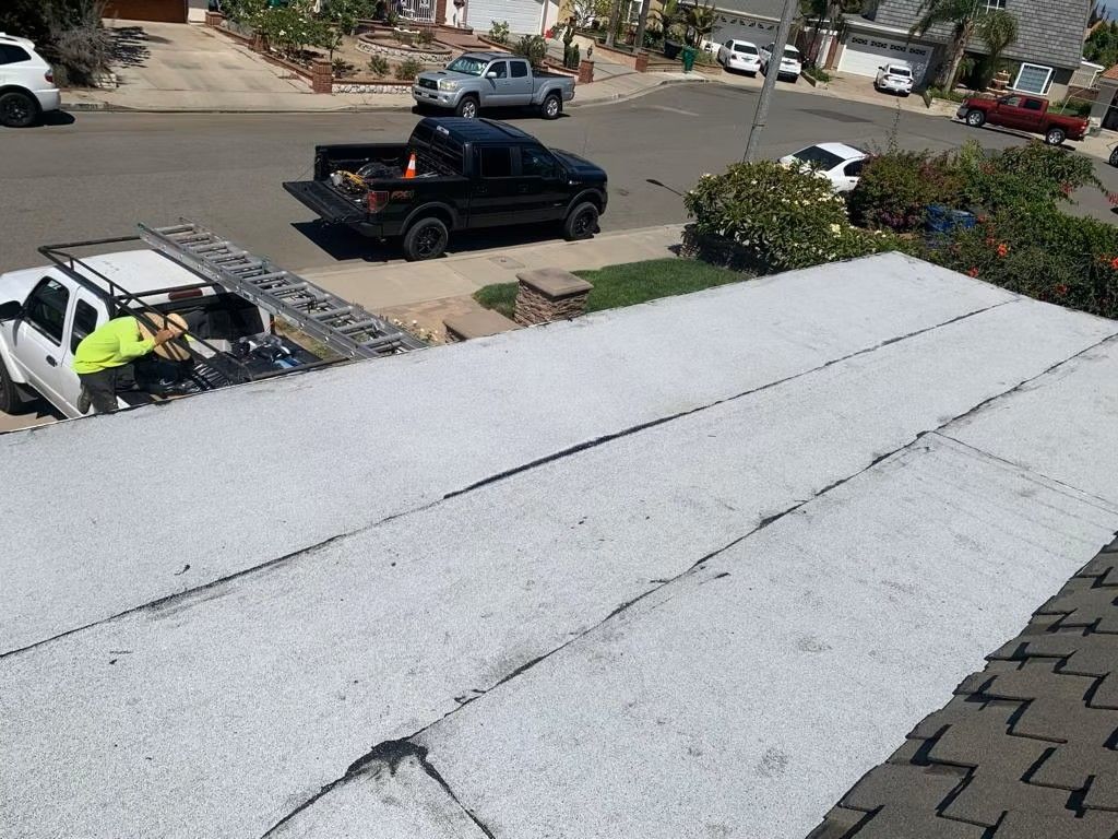 Roofing crew repairing a gray roof as a black pickup truck and curbside street are visible below