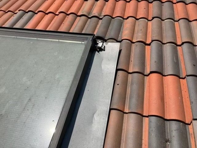 Roof tiles beside a glass skylight and metal flashing, with a small damaged area near the edge