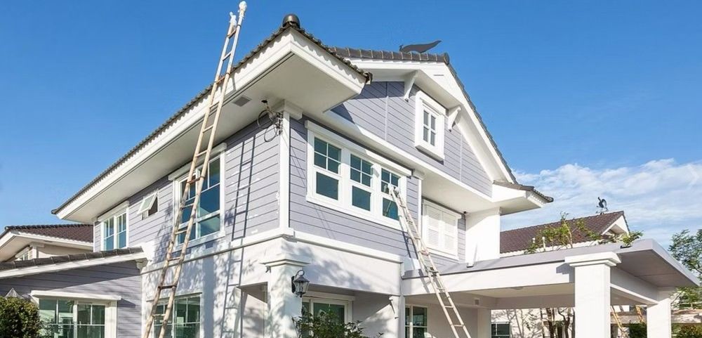 Two-story house under exterior renovation with ladders and white trim against a blue sky