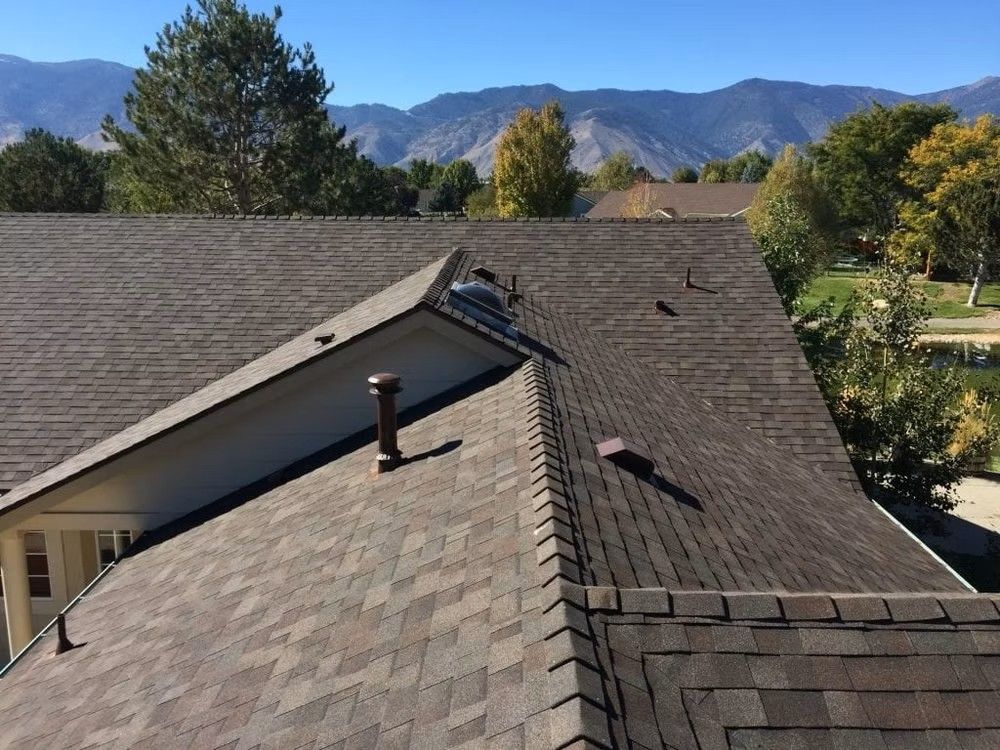 Roof with workers inspecting shingles, mountains and trees in the background