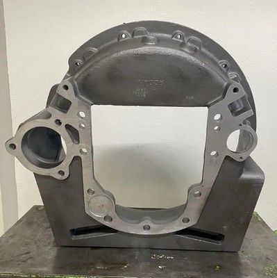 Una carcasa adaptadora de transmisión automotriz de metal gris con bridas de montaje, apoyada sobre un soporte.