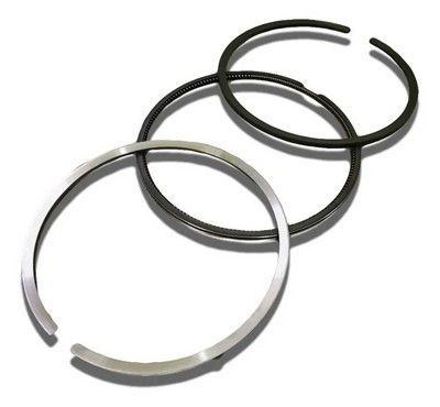 Tres anillos de pistón de motor, dos negros y uno plateado, dispuestos sobre una superficie blanca.