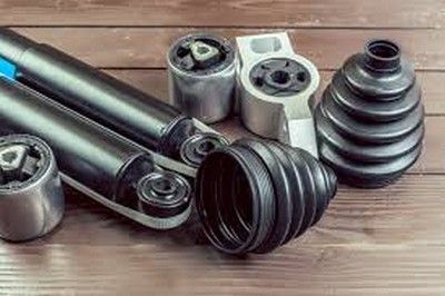 Piezas de suspensión de automóvil dispuestas sobre una superficie de madera: amortiguadores, bujes de goma y botas protectoras.