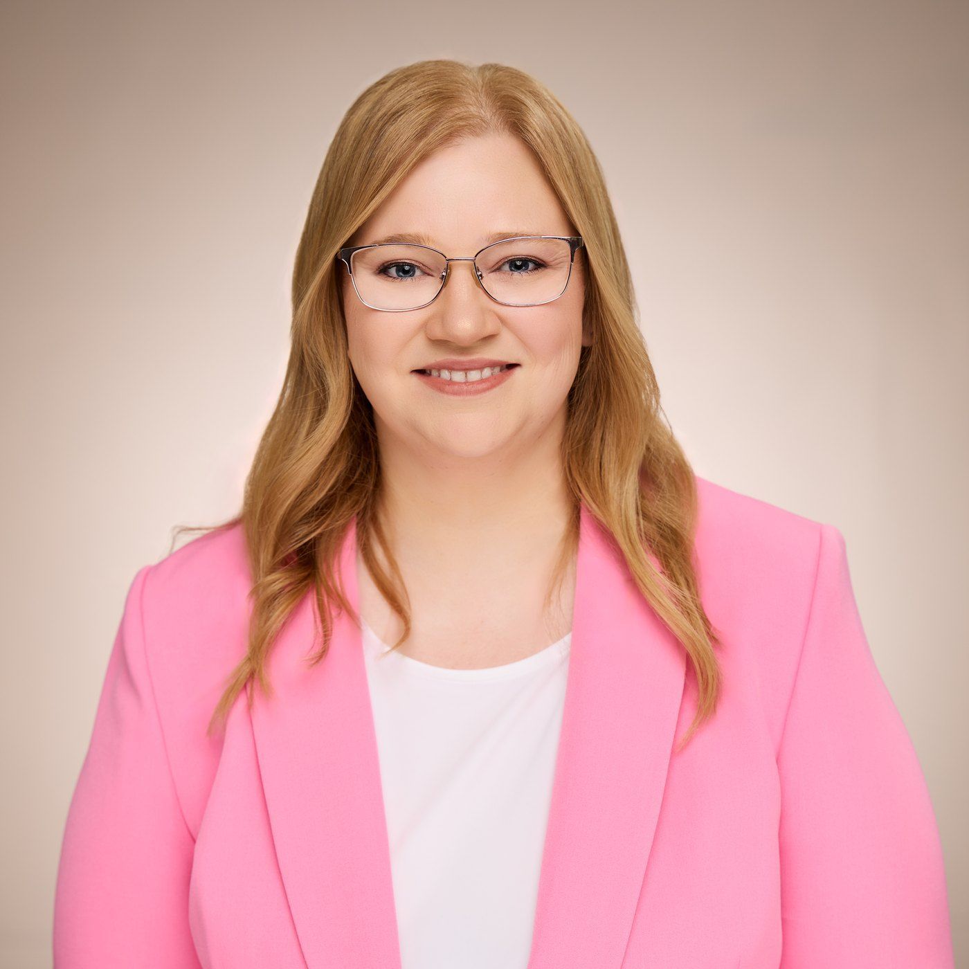 Smiling woman wearing glasses and a pink blazer against a neutral background