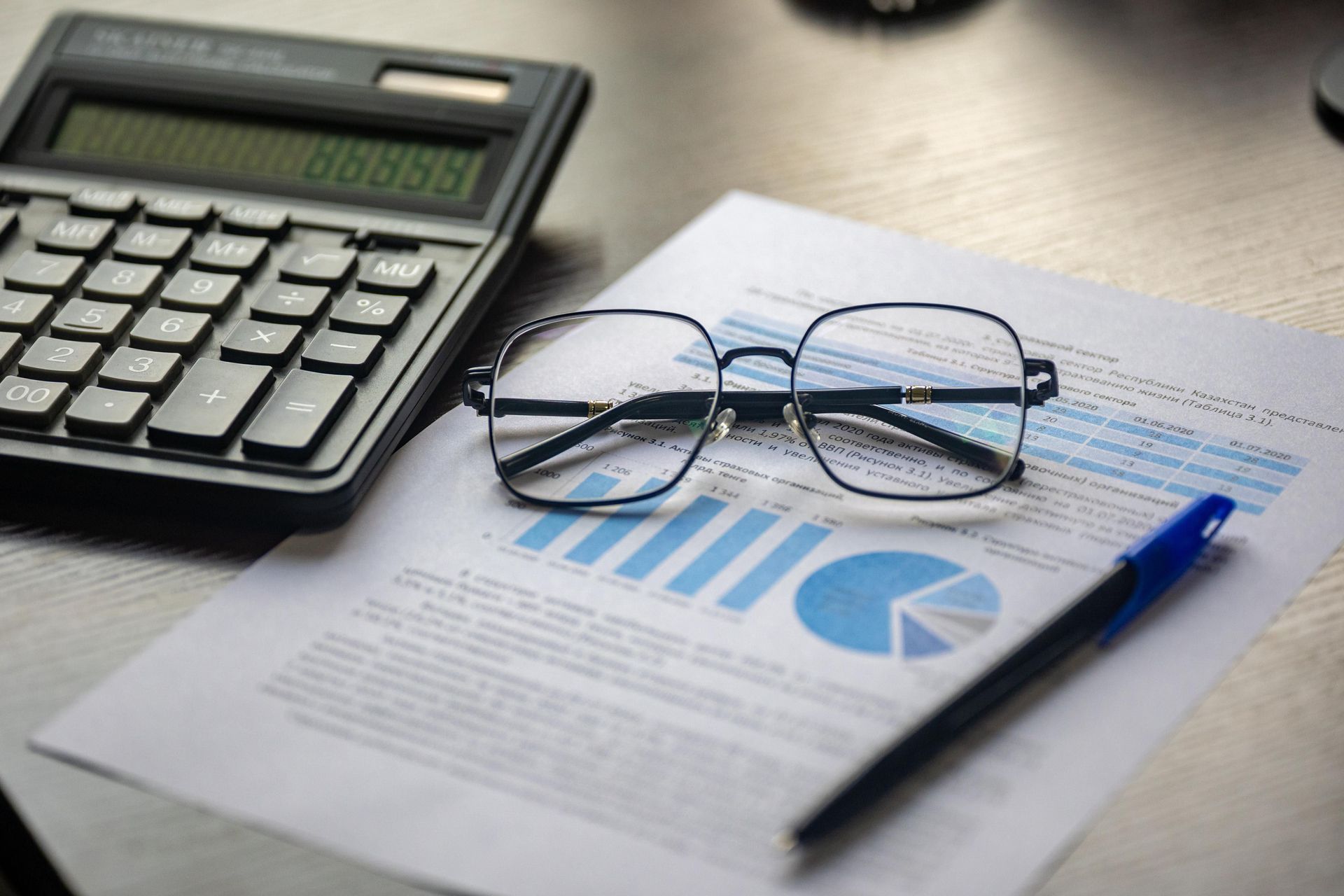 Calculator, eyeglasses, and pen on financial charts and papers on a desk.