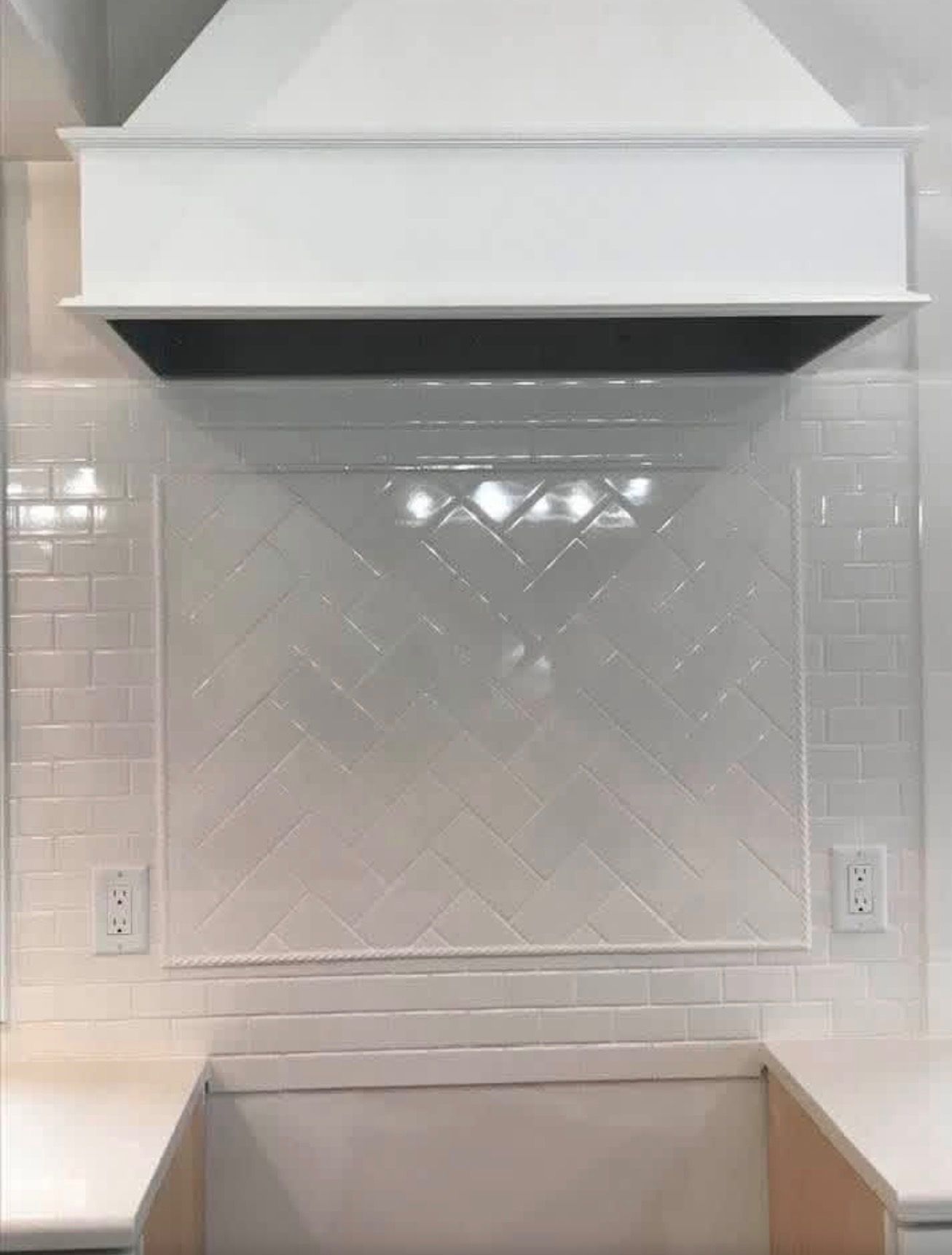 White kitchen backsplash with a central herringbone tile accent panel, framed by subway tiles under a white range hood.