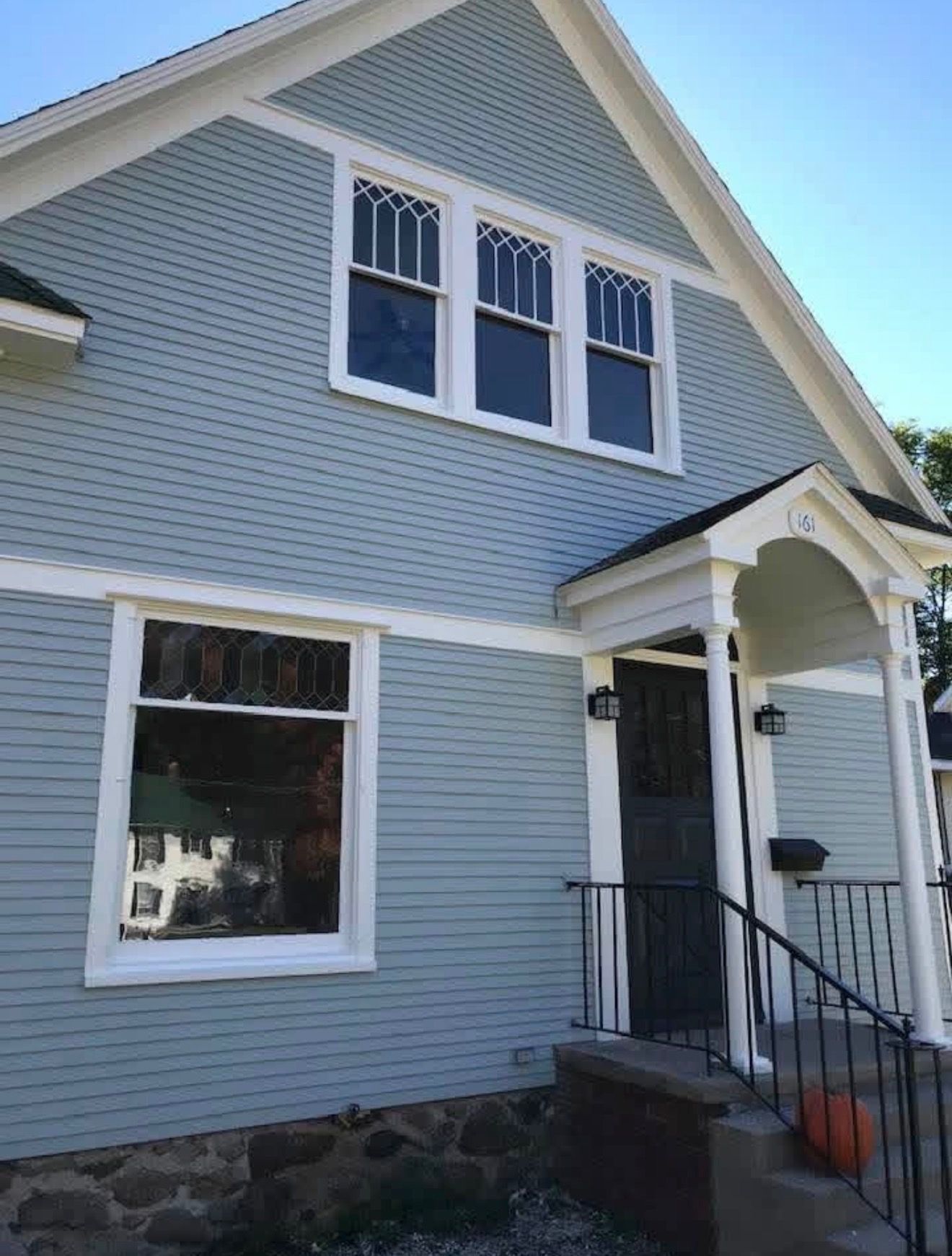 A light blue two-story house with white trim, a stone foundation, a front porch, and decorative windows.