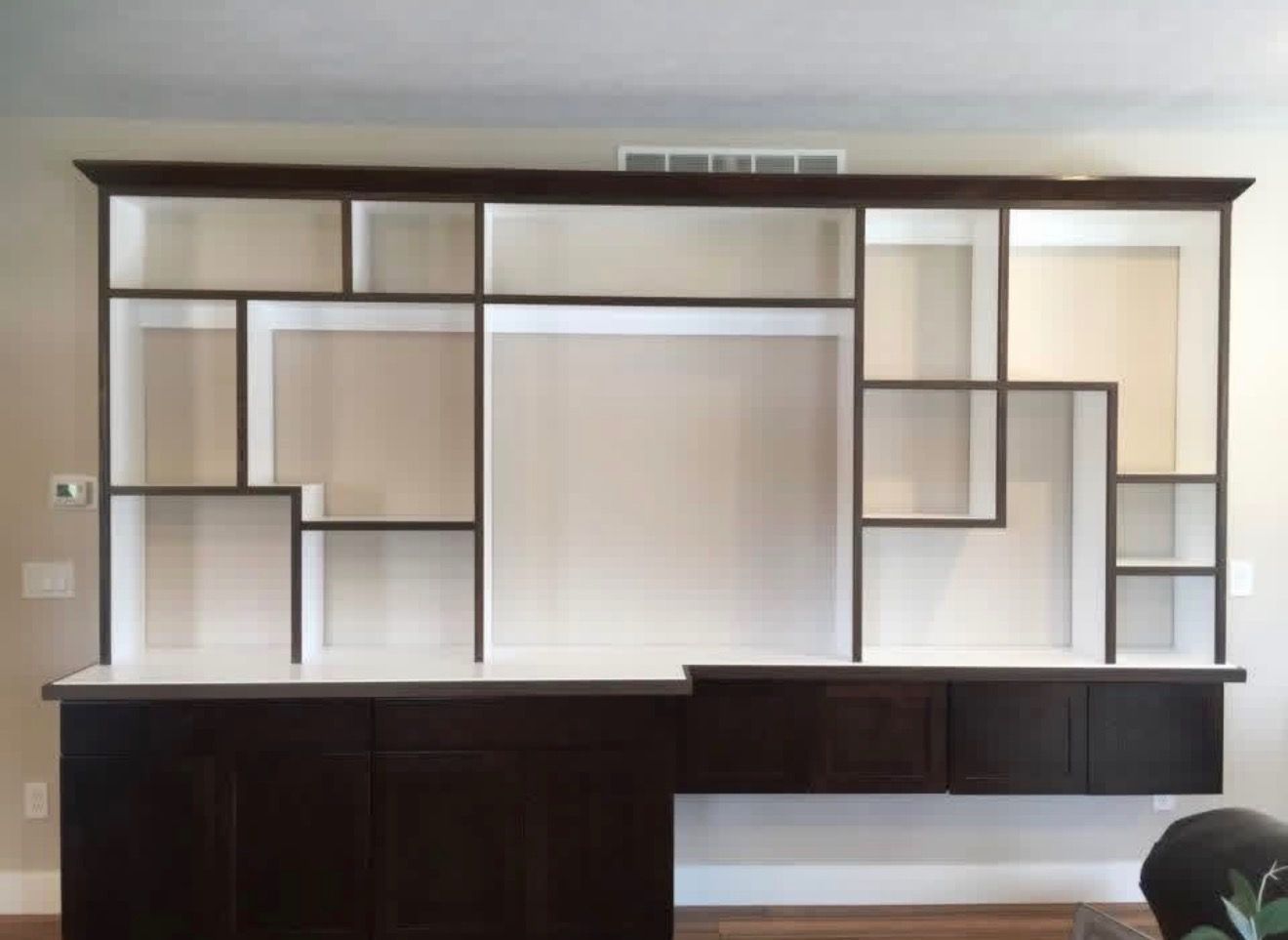 Custom dark wood and white wall unit with open shelving and lower base cabinets in a room with light-colored walls.