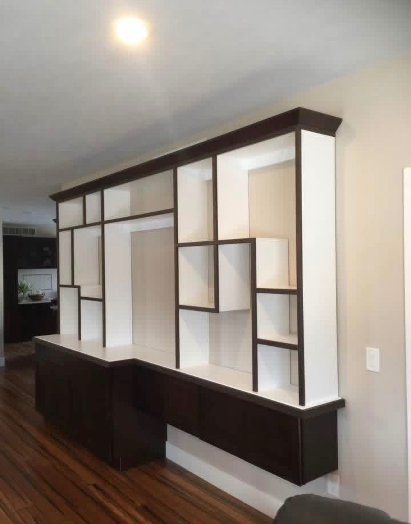 A floor-to-ceiling wooden wall unit featuring white open shelving with a dark brown frame, set against a light wall.