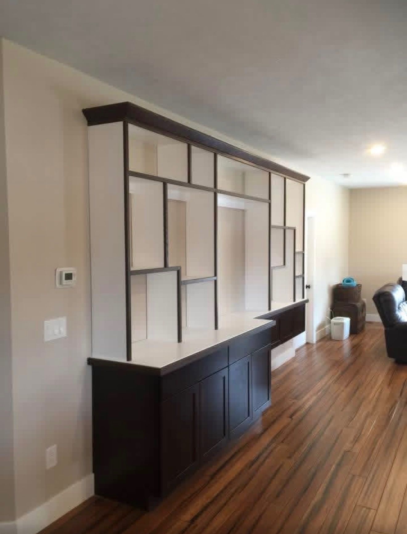 A wall-mounted display unit with a dark wood frame and white shelves above dark storage cabinets in a home interior.