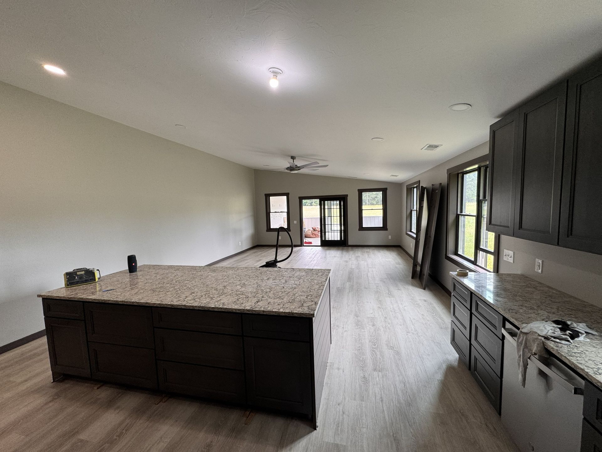 An open-concept kitchen and living area featuring dark cabinets, light granite countertops, and wood-look flooring.